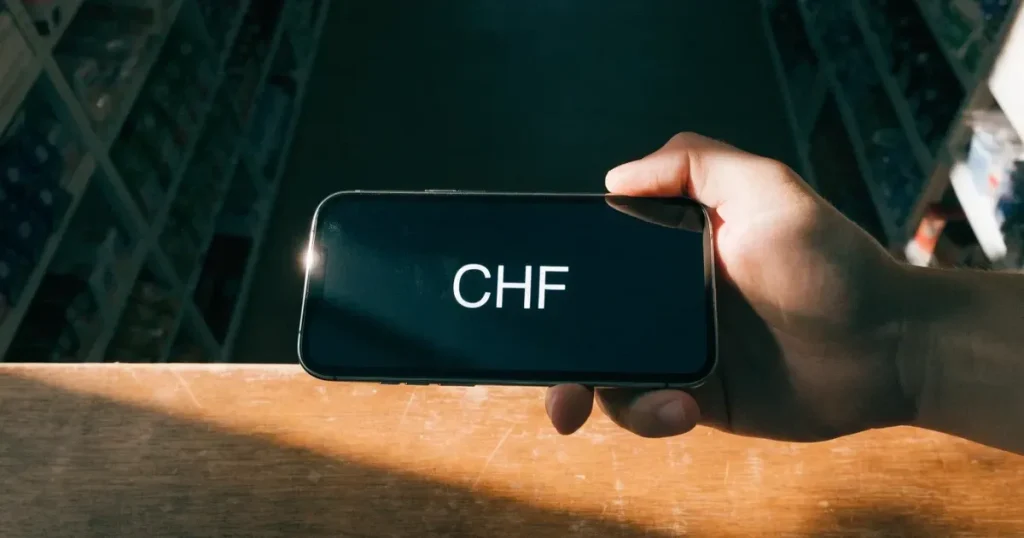 Eine Hand hält ein Smartphone mit dunklem Display knapp über eine hölzerne Ladentheke in einem kleinen Geschäft.