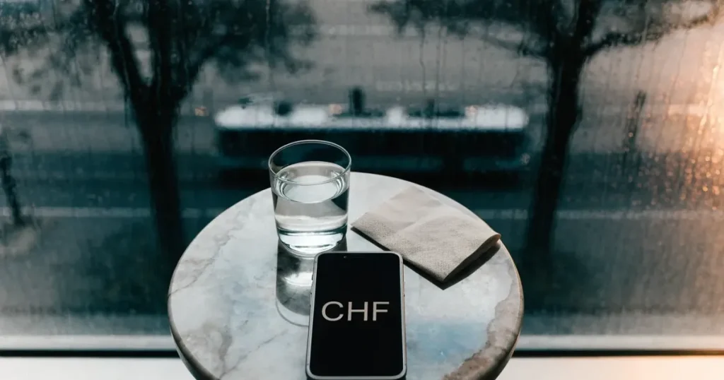 Ein Café-Tisch am Fenster trägt ein Smartphone mit dunklem Display, an der Scheibe laufen Regentropfen herunter und draussen steht eine Tram.