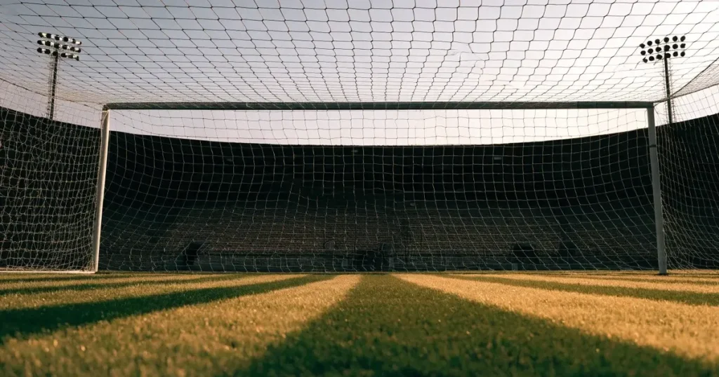 Ein Fussballtor mit weissem Netz steht auf frisch gemähtem Rasen, die hellen und dunklen Streifen im Gras leuchten im Gegenlicht.
