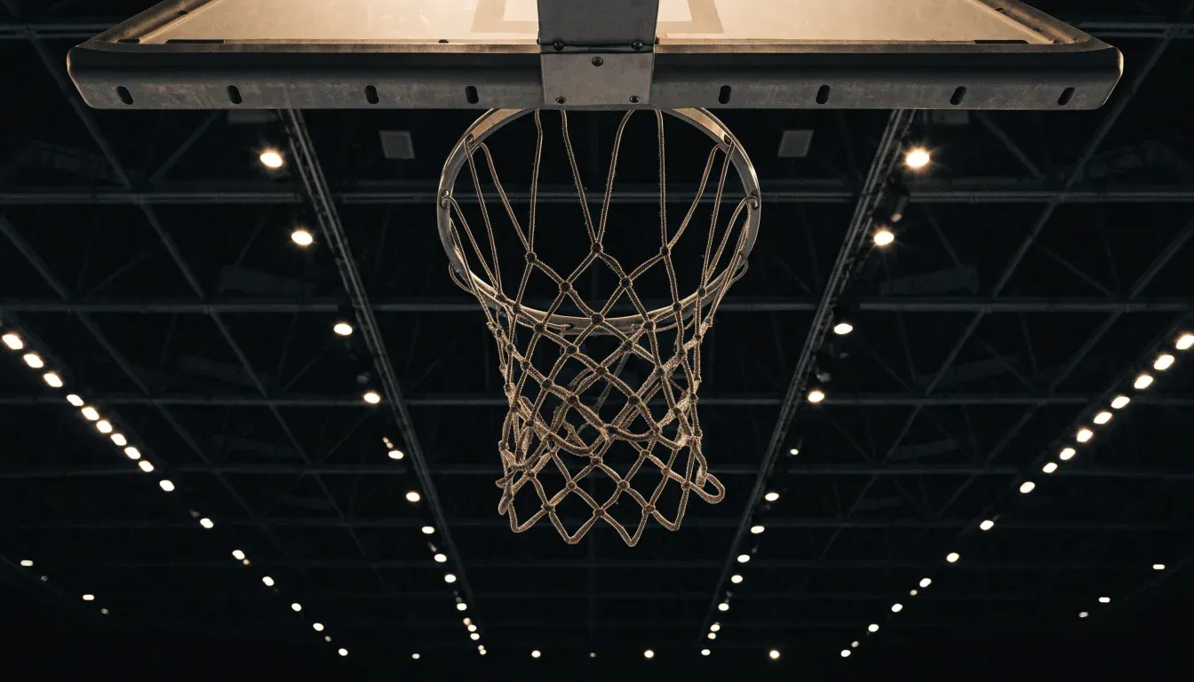Ein Basketballkorb von unten gesehen, darüber eine Hallendecke mit Scheinwerfern und Stahlträgern.