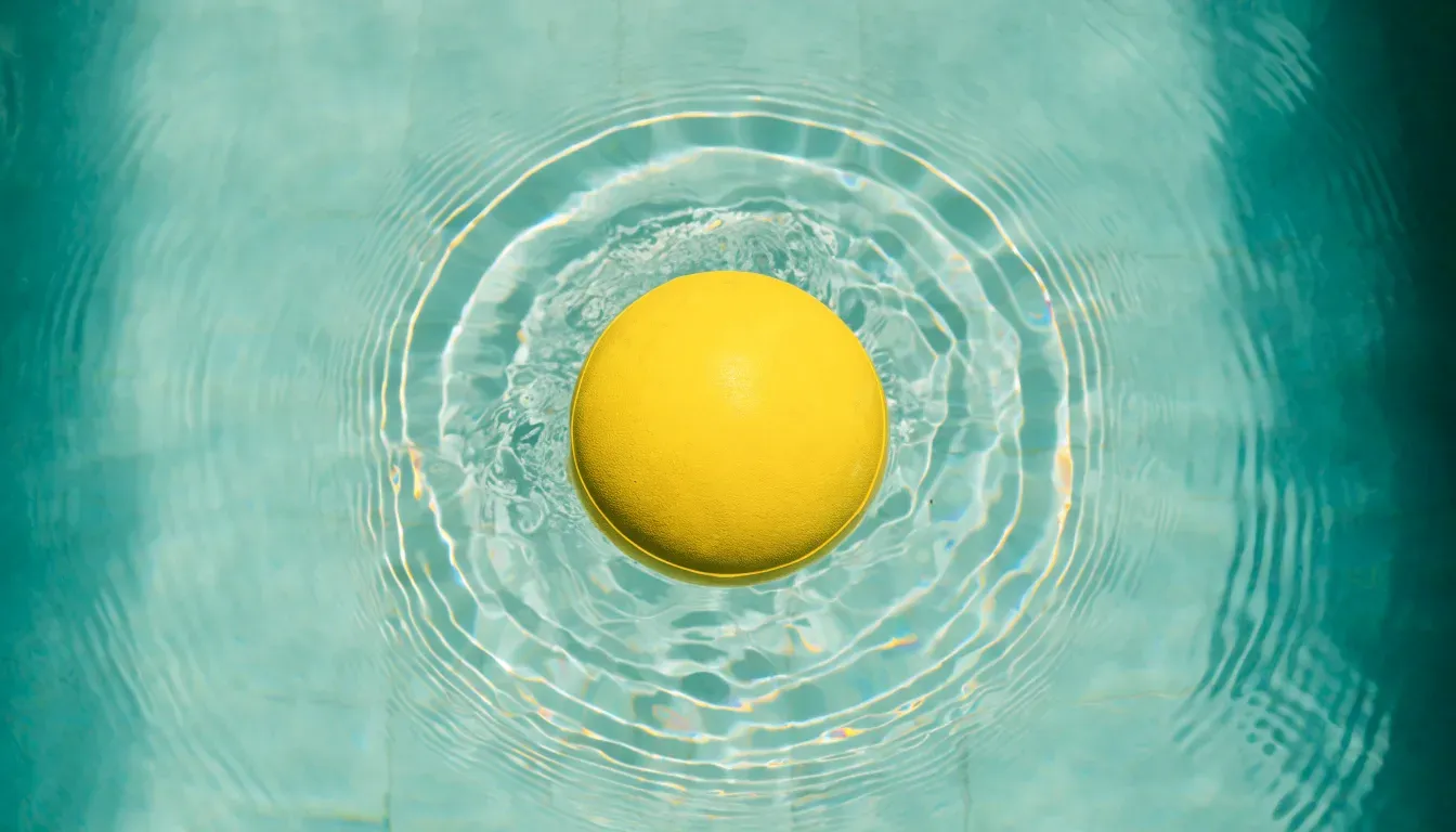 Ein gelber Ball treibt auf ruhigem türkisfarbenem Beckenwasser, feine Wellen im weichen Licht.