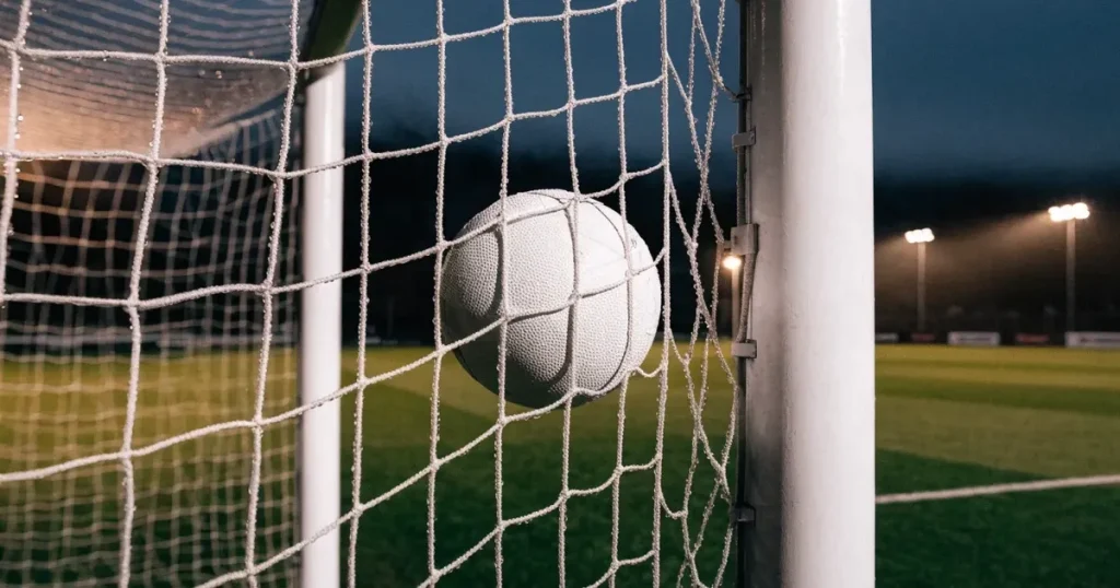 Ein Fussballnetz in Nahaufnahme, in dem ein Ball hängt, Wassertropfen glänzen auf den Maschen.