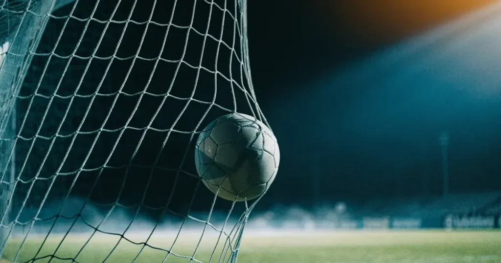 Ein Fussball liegt im Netz eines Tores, Flutlicht und kalte Abendluft liegen über dem leeren Platz